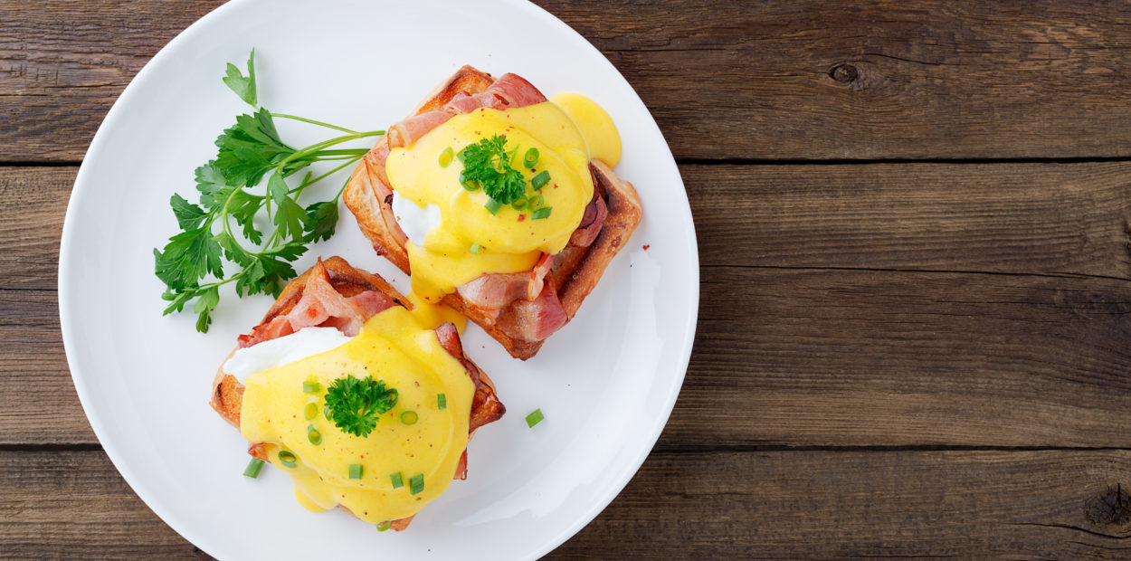 Eggs benedict with bacon on wooden background . Top view